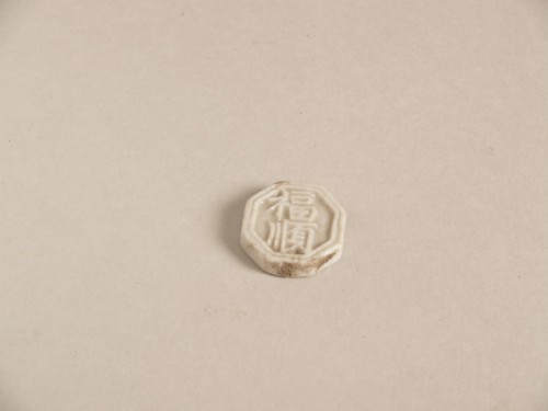 Miniatuurtegel, achthoekig, wit geglazuurd met blauw decor van Chinese karakters in reliëf